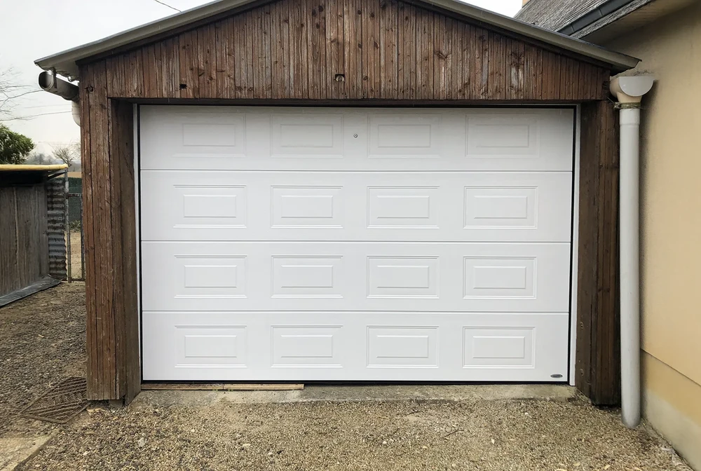 Porte de garage sectionnelle blanche installée dans structure bois